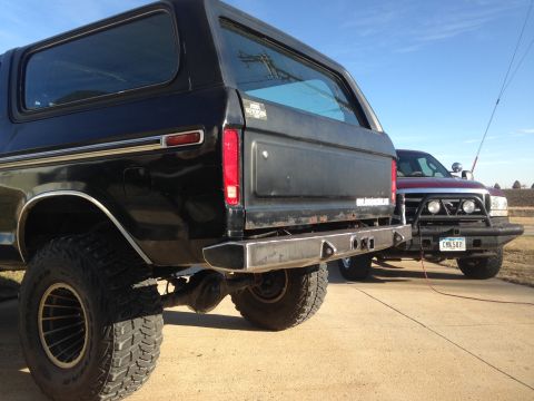 1979 Ford Bronco - Rear view of a black SUV with a custom bumper and large tires, parked on a paved surface next to another vehicle.