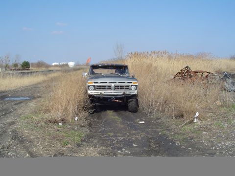 1979 Ford Bronco - Ford F-Series truck with lifted suspension on a dirt path, surrounded by dry grass.