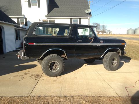 1979 Ford Bronco - A lifted black Ford Bronco is parked outside a residential garage on a sunny day.