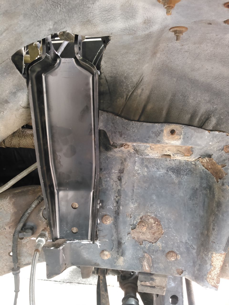 Black metal bracket installed on rusty vehicle frame with cut wheel well liner.