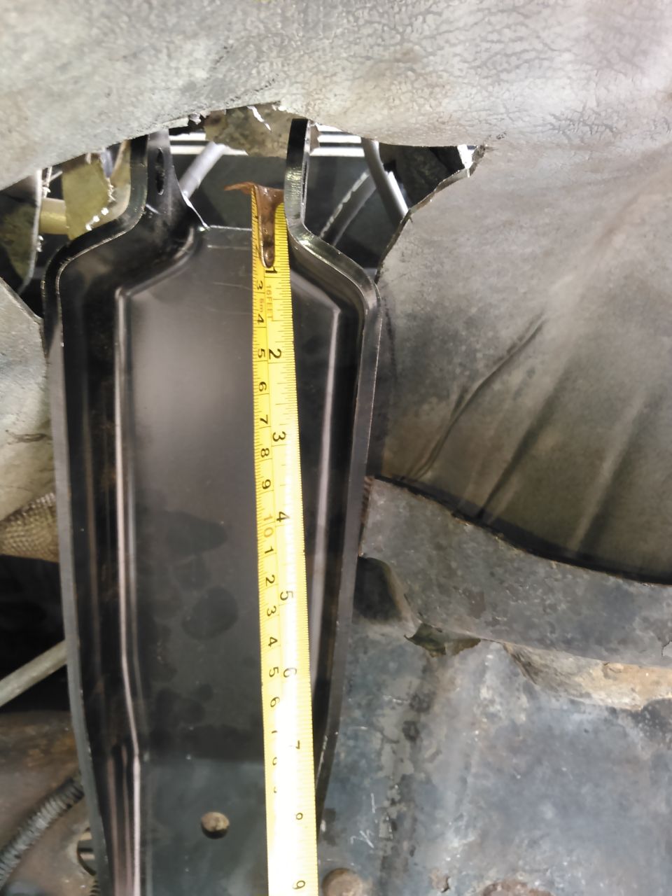 Close-up of a measuring tape on a black metal bracket under a vehicle.