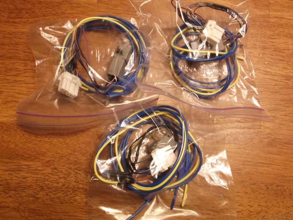 Three bags of wiring harnesses with connectors on a wooden table.