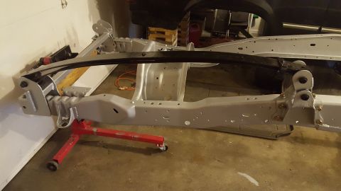 1994 Ford Bronco - The gray painted frame of a 1994 Ford Bronco is supported by a red engine stand. A black leaf spring is mounted above the frame.