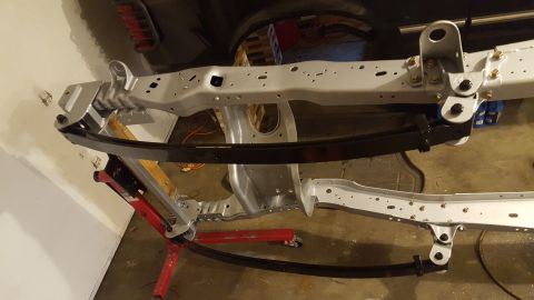 1994 Ford Bronco - A partially assembled vehicle frame with leaf springs is shown, supported by red jack stands. The frame appears to be painted light gray, a…