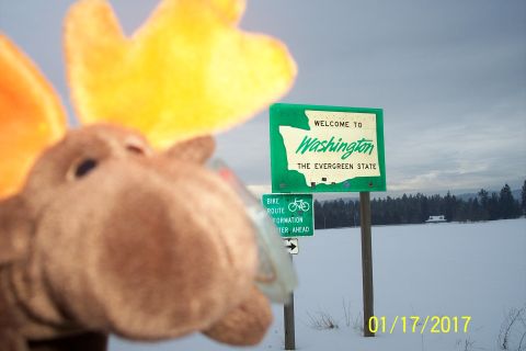 1989 Ford Bronco - A stuffed moose toy with orange and yellow antlers is in the foreground, obscuring part of a "Welcome to Washington" sign in a snowy landsc…