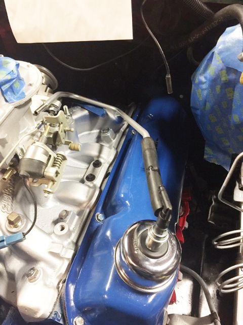 1978 Ford Bronco - A close-up view of a blue valve cover on a vehicle engine, with a spark plug wire connected to a spark plug. The engine bay also shows part…