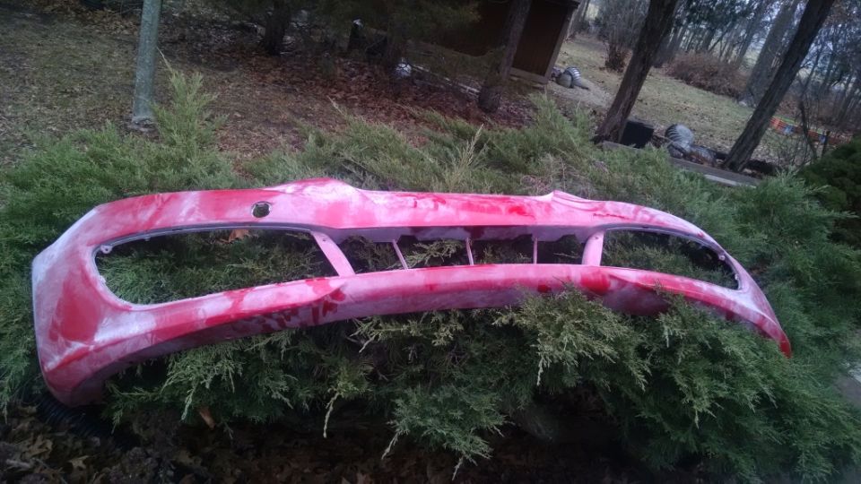Red car bumper with white primer/paint marks on green bushes
