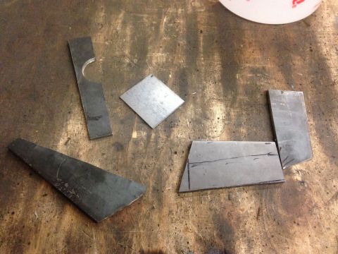 1979 Ford Bronco - Several pieces of cut metal are laid out on a dirty, wooden workbench. One piece is a long, thin rectangle with a curved notch removed from…