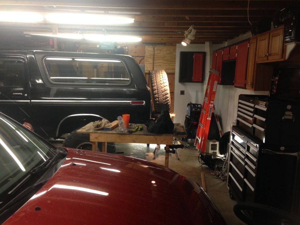 Black Ford Bronco parked in a garage with a red vehicle in the foreground.