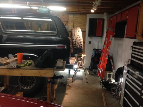 1979 Ford Bronco - The rear passenger side of a black Ford Bronco is parked in a garage. A workbench with tools and an orange cup is in the foreground.