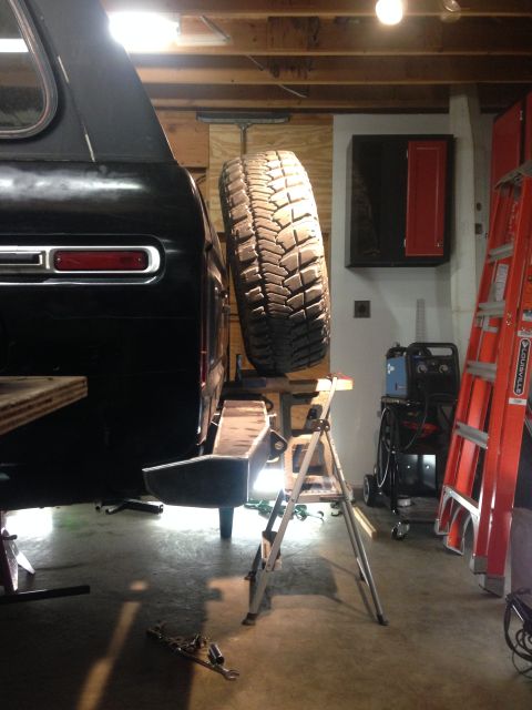 1979 Ford Bronco - The rear of a black SUV, possibly a 1979 Ford Bronco, is shown with a spare tire mounted externally. The vehicle is elevated on jack stands…
