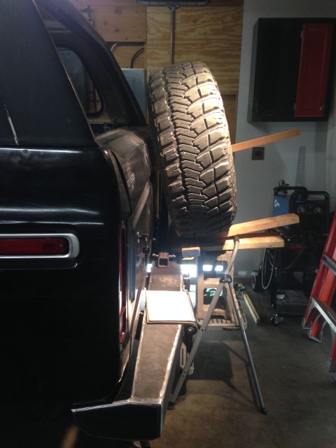 1979 Ford Bronco - The rear driver's side of a black SUV is shown with a large spare tire mounted to the back. The vehicle is in a garage setting with tools a…
