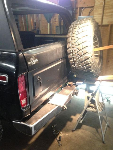 1979 Ford Bronco - The rear passenger side of a black Ford Bronco is shown with a spare tire mounted on the back. A custom metal bumper is being installed bel…