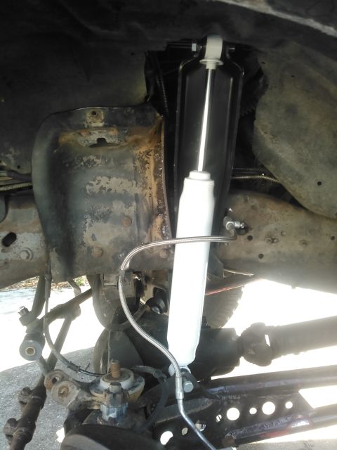 1996 Ford Bronco - A white and black aftermarket shock absorber is installed on the front suspension of a vehicle, connected by a braided metal line. The surr…