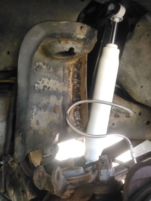 1996 Ford Bronco - A close-up view of the suspension system of a 1996 Ford Bronco, showcasing a white shock absorber and a heavily rusted metal bracket with v…