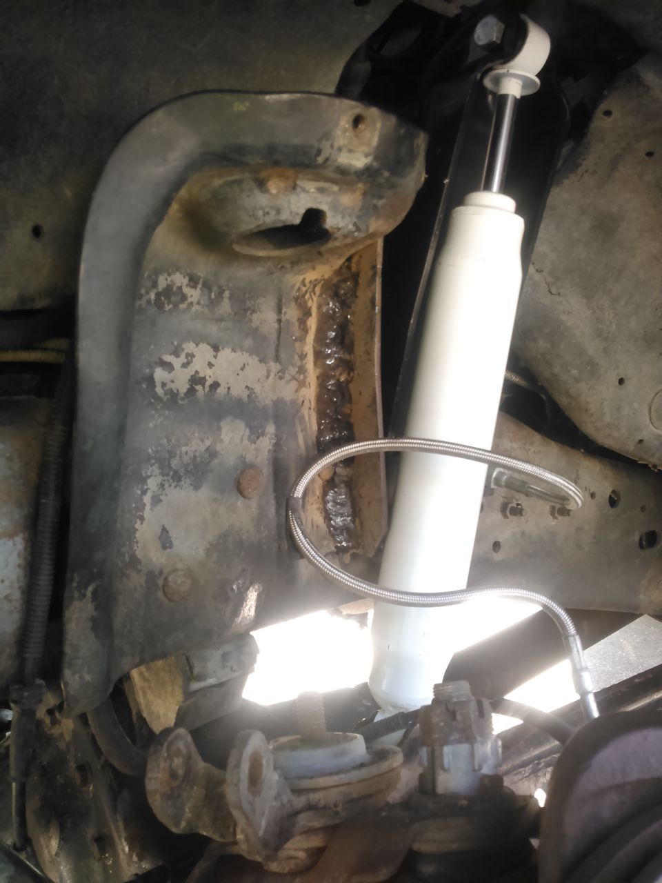 1996 Ford Bronco suspension with white shock and rusted bracket.