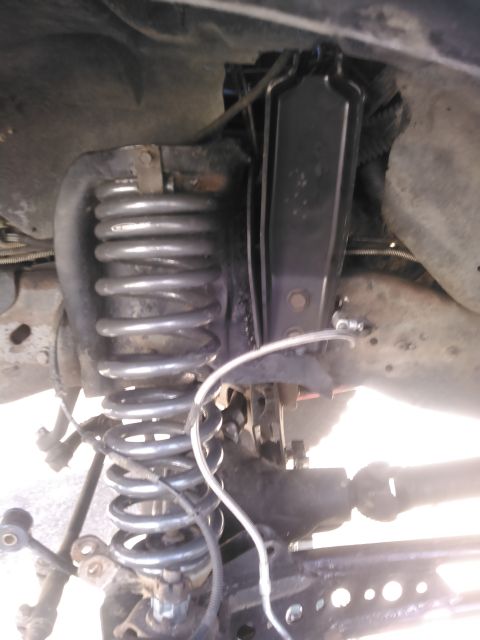 1996 Ford Bronco - A close-up view of the front suspension of a vehicle, showing a large coil spring, shock absorber, and part of the drive shaft. The compone…