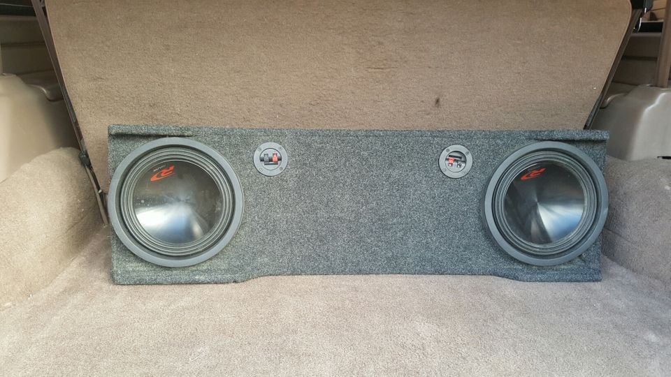 Dual 12-inch Alpine subwoofers in a grey carpeted box in a vehicle's cargo area.