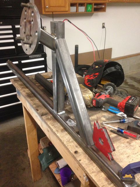 1979 Ford Bronco - A metal fabrication project is underway on a wooden workbench. The project includes a metal frame with a wheel hub assembly attached, along…