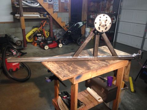 1979 Ford Bronco - A custom-fabricated metal trailer hitch assembly with a large, circular hub is resting on a wooden workbench in a garage setting. The assem…