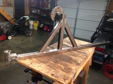 1979 Ford Bronco - Fabricated welded steel tubular bracket with bolt-on flange and pivot tube, clamped on a plywood workbench in a home garage.