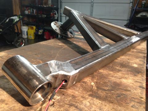 1979 Ford Bronco - A custom-fabricated steel suspension component, likely for a 1979 Ford Bronco, rests on a wooden workbench. The part features welded joints…