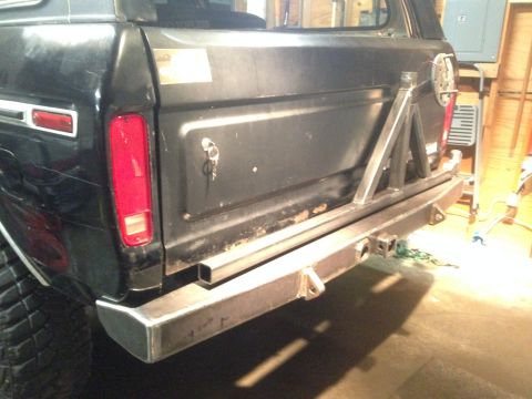 1979 Ford Bronco - The rear driver's side of a black SUV with a custom metal bumper and spare tire mount. The bumper has a hitch receiver and tow hooks visibl…