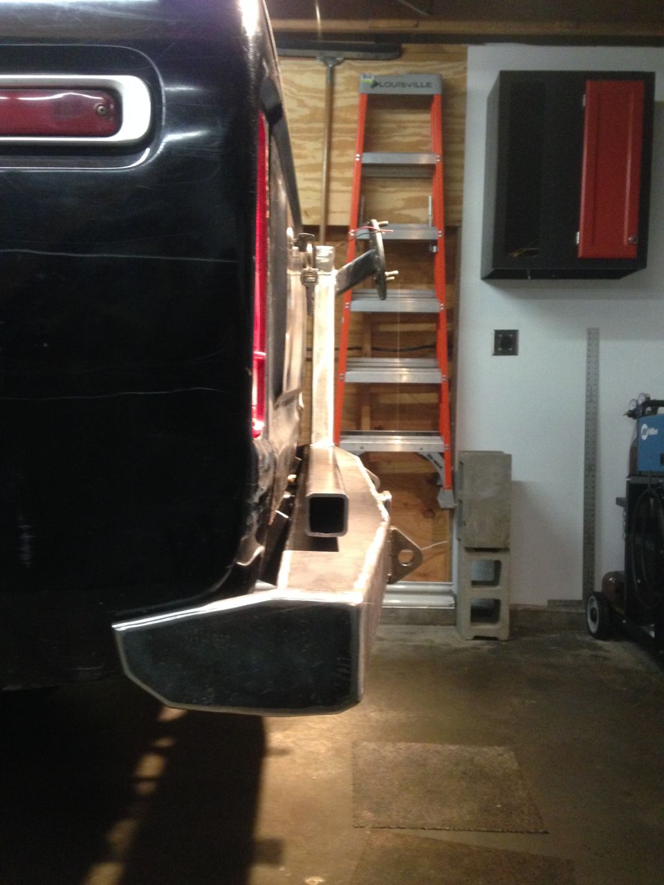Rear passenger side of a black vehicle with custom bumper, orange ladder in background.