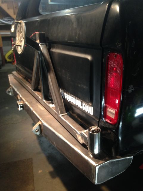 1979 Ford Bronco - The rear driver's side of a black Ford Bronco is shown with a custom steel bumper and a swing-away spare tire carrier. A red taillight and…