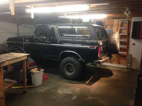 1979 Ford Bronco - A black Ford Bronco is parked in a garage, showing its side profile. The vehicle has large off-road tires and a spare tire mounted on the r…
