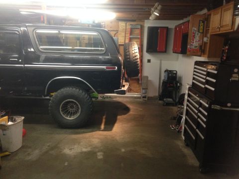 1979 Ford Bronco - The side view of a black Ford Bronco is parked in a garage next to a large toolbox and other equipment. A spare tire is mounted on the rear…