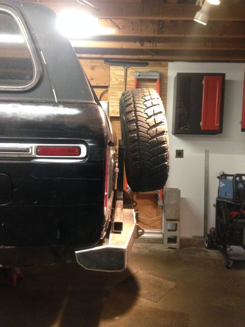 1979 Ford Bronco - The rear passenger side of a black SUV is shown, featuring a custom steel bumper with a mounted spare tire. The vehicle is in a garage sett…