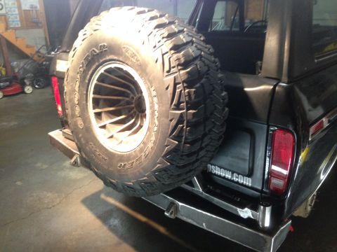 1979 Ford Bronco - The rear of a black Ford Bronco is shown with a large spare tire mounted on a swing-away carrier. A custom metal bumper is installed below…