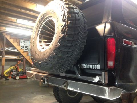 1979 Ford Bronco - The rear of a black Ford Bronco is shown, featuring a large spare tire mounted on the back and a custom metal bumper. A website address is…