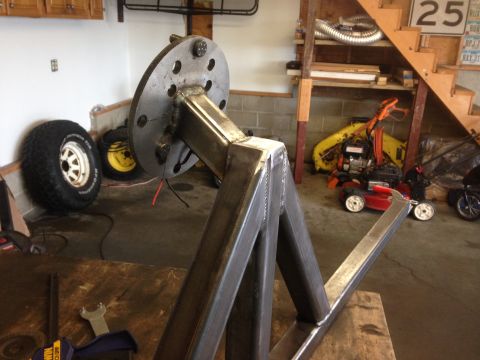 1979 Ford Bronco - A custom-fabricated steel stand with a wheel hub is shown in a garage setting. Visible in the background are two tires, lawn equipment, and…
