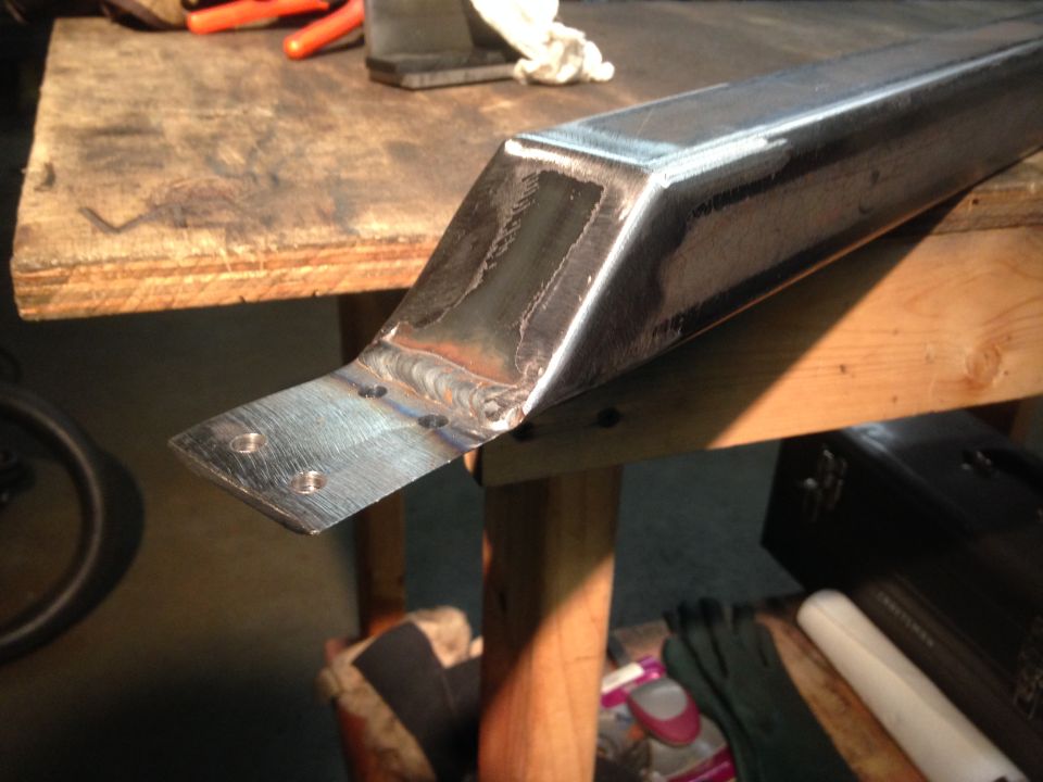 Metal bracket with welds and holes on a workbench.