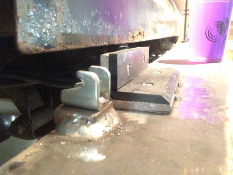 1979 Ford Bronco - A close-up view shows a metal bracket welded to a vehicle frame, with a U-shaped metal piece attached to it. A black rubber block with two…