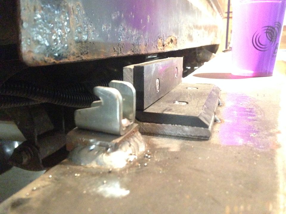 Welded bracket and U-shaped metal piece on vehicle frame, with rubber block and purple cup.