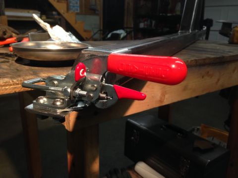1979 Ford Bronco - A close-up of a metal clamp with a red handle is attached to a metal frame on a wooden workbench.