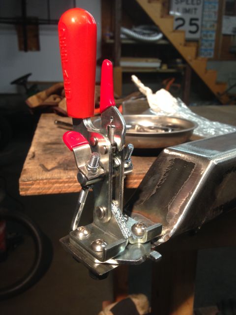 1979 Ford Bronco - A close-up of a toggle clamp with a red handle is attached to a metal bracket. The clamp is positioned over a piece of raw metal, possibly…