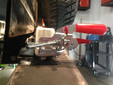 1979 Ford Bronco - A close-up view of a metal toggle clamp with red handles is attached to a welded metal bracket on what appears to be a vehicle frame. The c…
