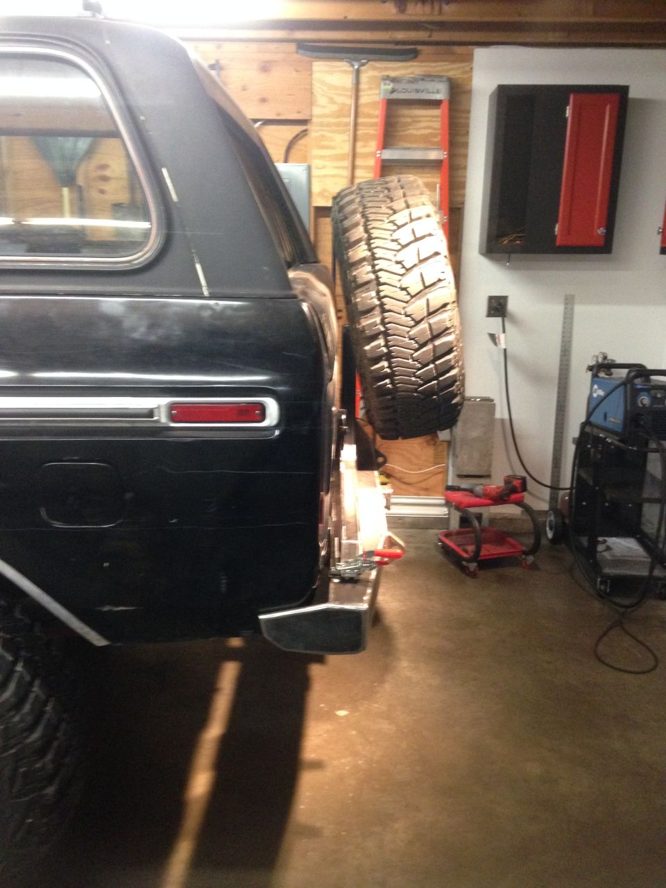 Black SUV with spare tire mounted on rear carrier in a garage.