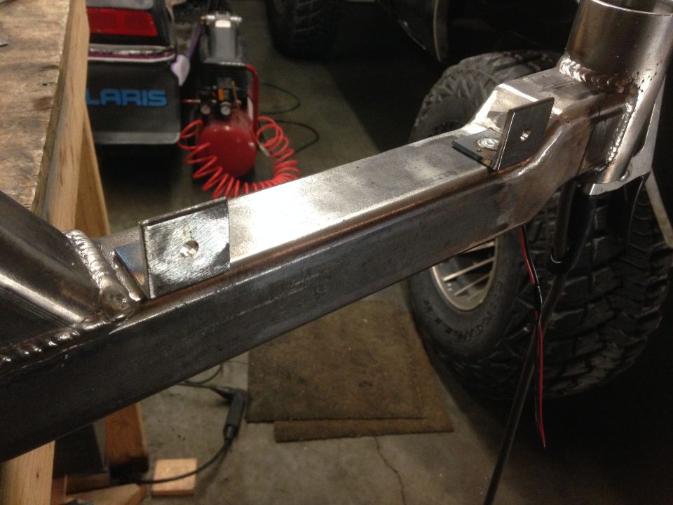 Close-up of custom metal vehicle frame with welds and brackets, tire and air compressor in background.