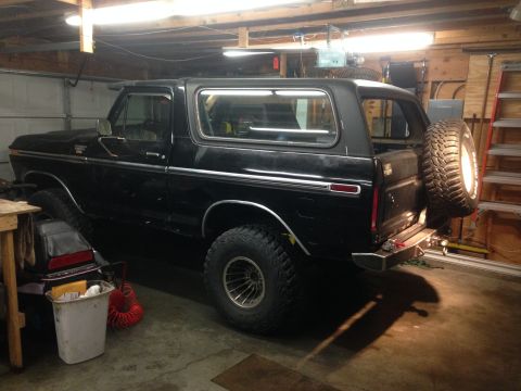 1979 Ford Bronco - A black Ford Bronco is parked in a garage, featuring a spare tire mounted on the rear tailgate and large off-road tires. The vehicle is vie…