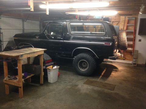 1979 Ford Bronco - A black Ford Bronco is parked in a garage with a spare tire mounted on the rear. A wooden workbench and a white trash can are in the foregr…