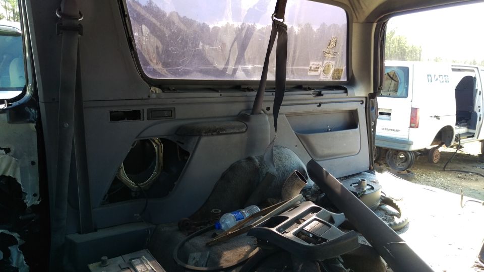 Interior of a disassembled Ford Bronco with a white Chevrolet van in the background.