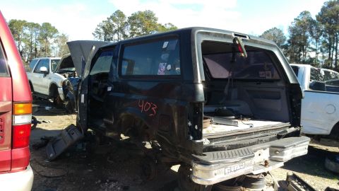 1994 Ford Bronco - The rear passenger side of a dark-colored Ford Bronco is shown in a junkyard setting. The vehicle is missing its rear quarter panel and has…