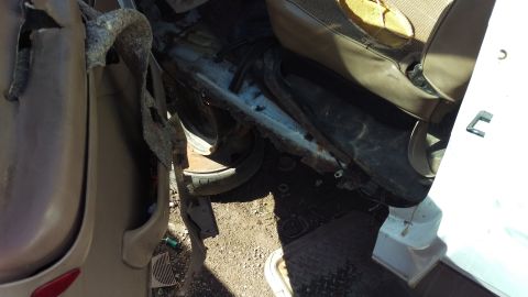 1994 Ford Bronco - The interior of a damaged vehicle shows a torn fabric seat and rusted metal framing. A tire is visible beneath the seat.