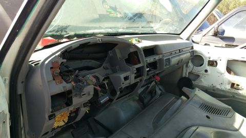 1994 Ford Bronco - The interior of a dismantled vehicle shows a gray dashboard with exposed wiring and components. A portion of the door frame and exterior ar…