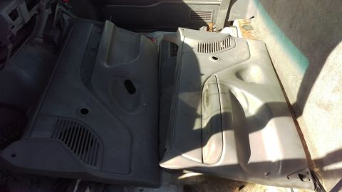1994 Ford Bronco - Two dark gray plastic interior door panels are laid out on the floor of a vehicle. The panels have molded sections for speakers and door ha…
